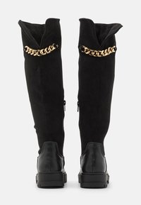 Botas negras de ante hasta la rodilla con un acento de cadena metálica dorada, con punta redonda y suela de goma para mayor tracción.