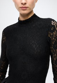 Black lace top with long sleeves and a high neck. Features a floral pattern and sheer details on the arms, showcasing intricate texture and design.
