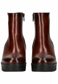 Bottes de cheville en cuir marron avec une texture lisse, dotées d'une fermeture éclair sur le côté et d'une semelle noire robuste. La forme est épurée et ajustée.