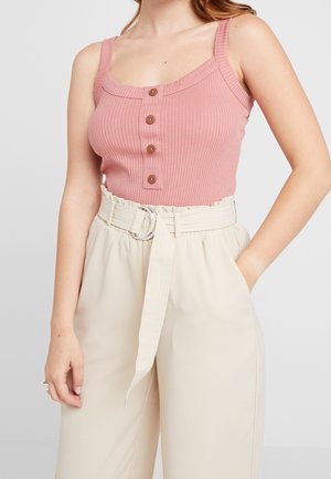 Różowy prążkowany top na szerokich ramiączkach, z okrągłym dekoltem i pięcioma brązowymi guzikami, zestawiony z kremowymi spodniami z paskiem.