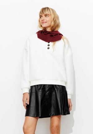 Sweatshirt en polaire blanc avec un col montant, trois boutons et des poignets côtelés, associé à une jupe en cuir noir de coupe évasée.