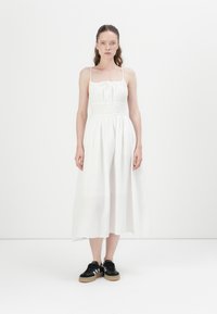 Hvit, ermeløs maxikjole med samlet midje og subtil tekstur, kombinert med svarte joggesko med hvite striper og gummi såler.