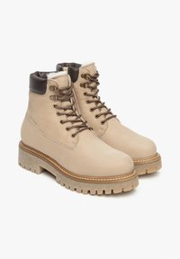 Bottines en cuir beige avec des accents marron, à bout rond et semelle en caoutchouc texturée. Comprend des œillets en métal et des lacets pour un maintien sécurisé.
