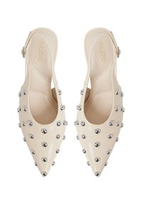 Beige kiilto-nahka slingback-korkokengät terävillä varpailla, joissa on metalliset hopeiset niitit sivuilla ja pieni nilkkahihna.