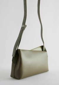 Olivengrüne Lederhandtasche mit einem strukturierten, kantigen Design, flacher Oberfläche und verstellbarem Tragegurt, ausgestattet mit einer glatten Textur und klaren Linien.