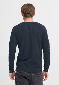 Marineblauwe trui met lange mouwen van zachte stof, met een ronde halslijn en geribde boorden en zoom, weergegeven vanaf de achterkant.