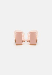 Paire de sandales à talons hauts rose blush avec brides transparentes sur le dessus, vues de dos sur fond blanc.