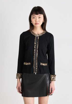 Black cardigan with leopard print accents at the collar, pockets, and cuffs. Features a zip closure and long sleeves. Worn over a black leather skirt.