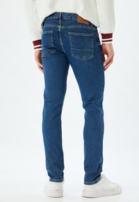 Niebieskie dżinsy w slim fit, z klasycznym pięciopocketowym wzorem i skórzaną naszywką na pasku. Gładka faktura i średnie pranie.