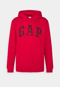 Sudadera roja con un bolsillo delantero y capucha con cordón. Presenta un gran logo negro de "GAP" en el pecho. Hecha de tela suave.