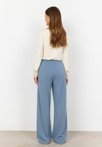 Pantaloni a gamba larga in tessuto azzurro chiaro, con vita elasticizzata e texture morbida. Maglietta a maniche lunghe con dettagli in pizzo color crema.