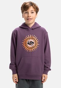 Lila hoodies med en stor solgrafik i orange och svart på framsidan, med en central ficka och standardpassform. Mjuk tygtextur.