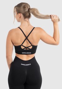 Sostén deportivo negro con tirantes cruzados en la espalda y detalle del logotipo. Combinado con leggings negros de talle alto que presentan el logotipo a juego. Textura suave.