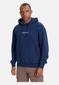 Felpa con cappuccio blu navy con tasca a canguro, cappuccio con coulisse e logo bianco "GUESS JEANS" centrato. Polsini e orlo a coste. Tessuto morbido.