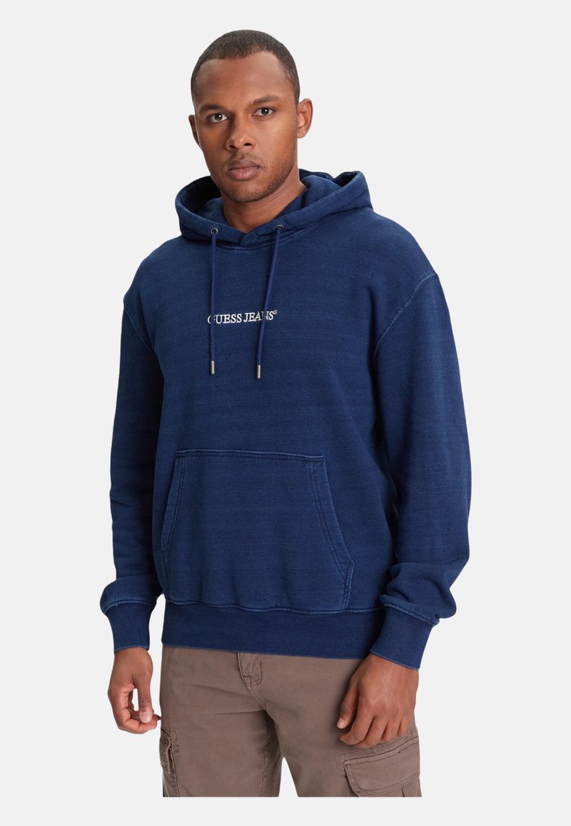 Felpa con cappuccio blu navy con tasca a canguro, cappuccio con coulisse e logo bianco "GUESS JEANS" centrato. Polsini e orlo a coste. Tessuto morbido.