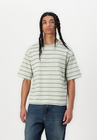 Camiseta de manga corta a rayas verdes y blancas con un ajuste relajado; textura suave; cuello redondo; combinada con jeans azul oscuro.