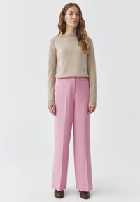 Lichtbeige, langemouwentrui gecombineerd met roze, hoge taille, wijde broek. Glad textiel met subtiele stikdetails en bruine schoenen.