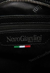 Interni in pelle nera con una zip argento, caratterizzati dall'etichetta "NeroGiardini" e da un piccolo emblema della bandiera italiana. Sfondo in tessuto morbido.
