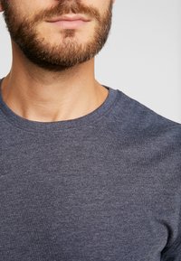 Marineblå t-skjorte med rund hals laget av myk, teksturert stoff, med en glatt halslinning og et minimalistisk design uten mønstre eller aksenter.