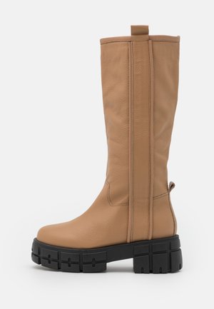 Botte haute en cuir couleur fauve avec bout arrondi et semelle épaisse noire et robuste, dotée de languettes de traction en haut et à l'arrière de la tige.