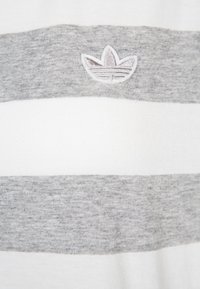 Vit och grå randig skjorta i mjuk bomull; har en broderad trebladig logotyp i övre vänstra hörnet.