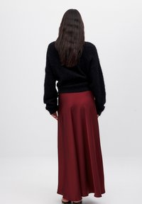 Schwarzer, flauschiger Pullover und ein langer, fließender Rock aus burgunderrotem Satin mit glatter Textur. Rückansicht, minimale Hardware oder Akzente sichtbar.