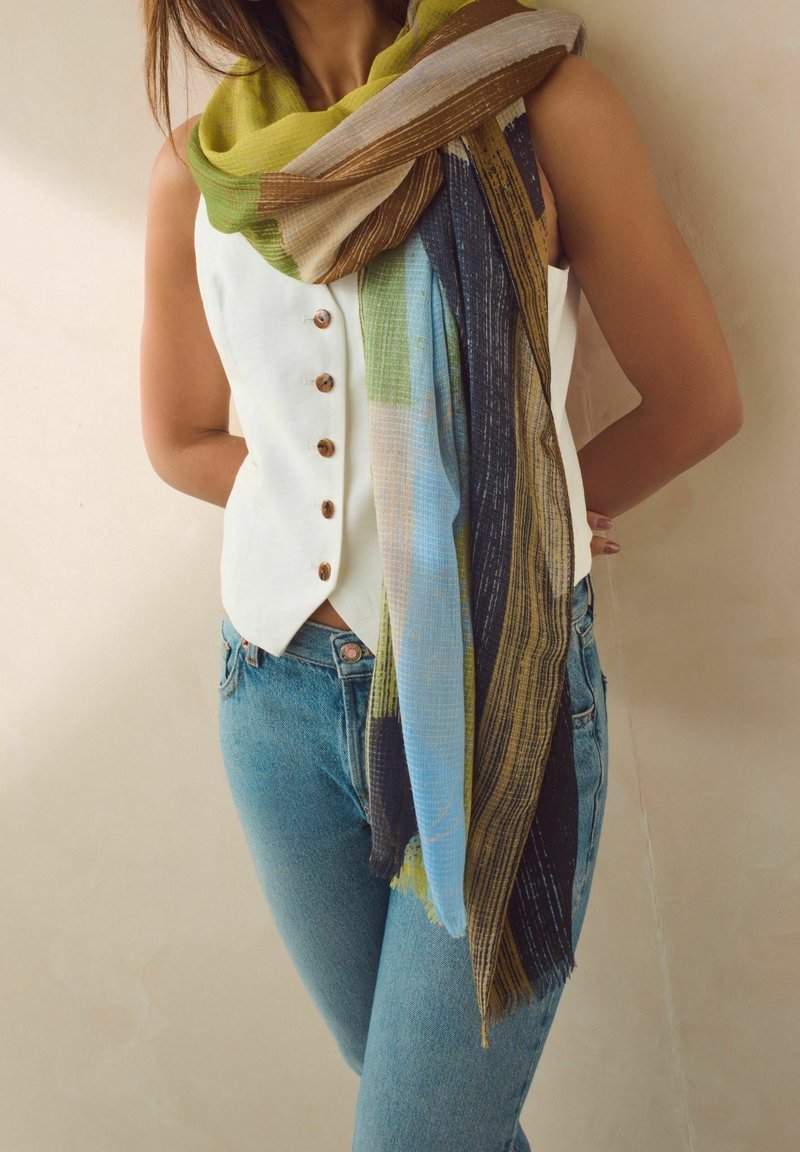 Femme portant un gilet sans manches blanc boutonné, un jean bleu et une écharpe multicolore drapée autour du cou et des épaules.