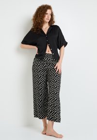 Haut noir à manches courtes avec fermeture à boutons, associé à un pantalon court noir décontracté avec des pois blancs, en tissu lisse, coupe relaxée.