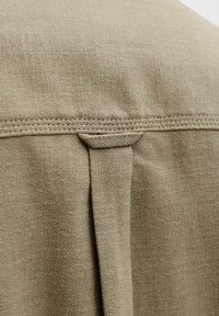 Tela de color verde oliva con un tejido texturizado, que presenta una costura reforzada en el hombro y un pliegue vertical para mayor detalle.