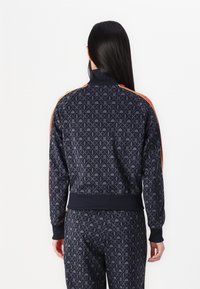 Navy track jacket with all-over geometric pattern, high collar, ribbed cuffs, and orange side stripes. Made from soft fabric with a fitted silhouette.
