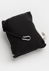 Zwarte vierkante kussen met een gladde textuur, uitgerust met een zilveren karabijnhaak die aan een stoffen riem is bevestigd, en een label met schaarontwerp.