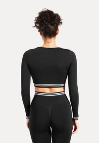 Sort cropped langærmet top med hvide stribede accenter ved kanten, parret med sorte højtaljede leggings. Glat tekstur.