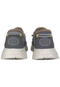 Grijze stoffen sneakers met beige accenten, voorzien van een gespikkelde witte zool en een ronde logo op de hiel. Trekflappen in geel en grijs.