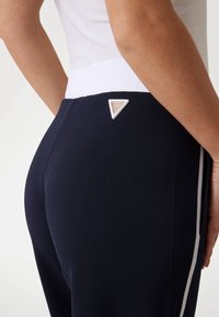 Navy-Hosen mit einem weißen Bund, strukturiertem Stoff und einem dreieckigen Logo-Akzent an der Rückseite. Seitenstreifen in kontrastierender Farbe.