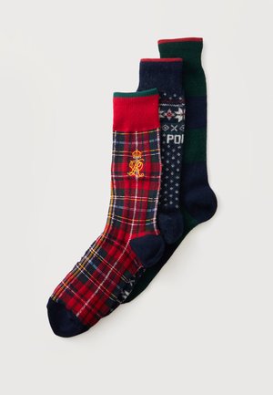 Trois paires de chaussettes de style montantes à motifs, à carreaux rouges, fair isle bleu marine et rayures vertes et bleu marine, disposées en chevauchement sur un fond clair.