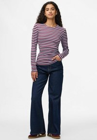 Camisa de rayas rojas y blancas de manga larga con cuello redondo, combinada con vaqueros acampanados de color azul oscuro y zapatillas de deporte marrones.