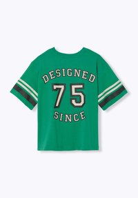 T-shirt en coton vert avec un col rond, des manches courtes et le texte imprimé "CONÇU 75 DEPUIS" avec des accents rayés contrastés sur les manches.