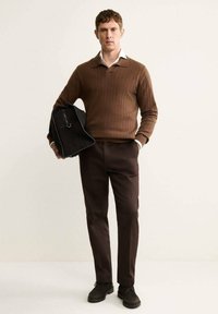 Maglione marrone a coste, camicia bianca con colletto sotto, pantaloni marroni scuri, borsa nera e scarpe scure. Design minimalista con colori neutri.
