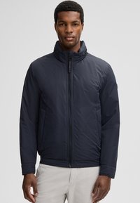 Donkerblauwe gewatteerde jas met een hoge kraag, ritssluiting aan de voorkant, zijzakken en een gladde, matte textuur. Met elastische manchetten.