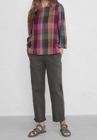 Top a scacchi multicolore nelle tonalità di rosa, verde e blu, con maniche a tre quarti. Abbinato a pantaloni grigi con risvolto e sandali.