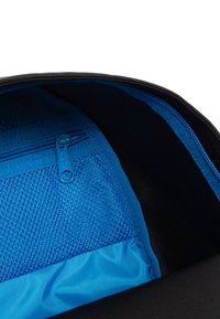 Intérieur d'un sac à dos noir avec une poche en maille bleue zippée et une section en tissu bleu lisse. Détails de piqûre contrastante visibles.