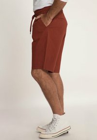 Red cotton shorts with an elastic waistband, side pockets, and a relaxed fit, paired with white high-top sneakers.