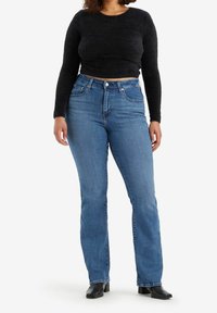 Jean en denim bleu taille haute avec une jambe droite, associé à un pull court noir en peluche, à manches longues et col rond.