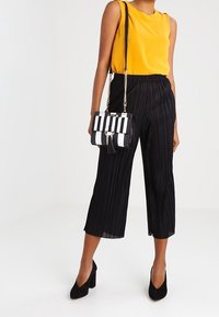 Top giallo senza maniche, culotte plissettate nere, tacchi alti neri e una borsa a righe con catena dorata e dettaglio a frange.