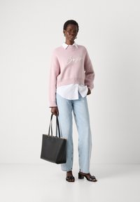 Lys rosa kort genser med "Boss" brodert i hvitt, lagd over en hvit skjorte med krage; kombinert med lyseblå jeans og svart totebag.