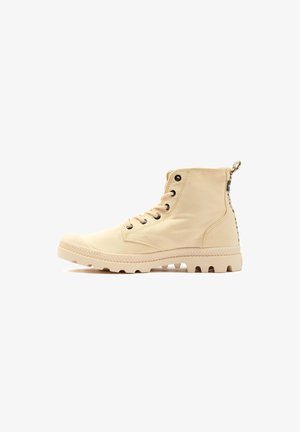 Bottines en toile beige avec une semelle en caoutchouc texturée, œillets en métal noir et une languette à l'arrière. Présente un design à bout rond.