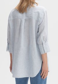 Ljust blå randig skjorta i mjukt tyg, med en avslappnad passform, uppvikta ärmar och en rundad nederkant. Synliga vertikala ränder.