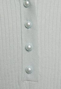 Vaaleanvihreä ribbitekoinen neulepaita, jossa on viisi pyöreää helmeä nappisarakkeessa ja sileä neulottu pinta.