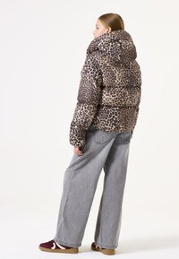 Veste en duvet imprimé léopard avec un col haut, rembourrée de duvet, et texture douce, associée à un jean large gris et des baskets bordeaux.