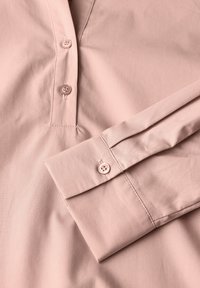 Camicia a maniche lunghe rosa pallido con abbottonatura, dotata di una texture liscia e polsini. Tessuto leggero e morbido con dettagli di cucitura discreti.